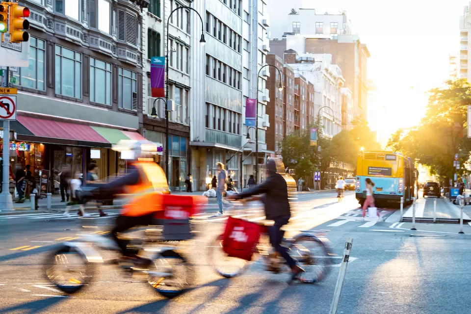 Two delivery bikes riding through intersection in New York City.